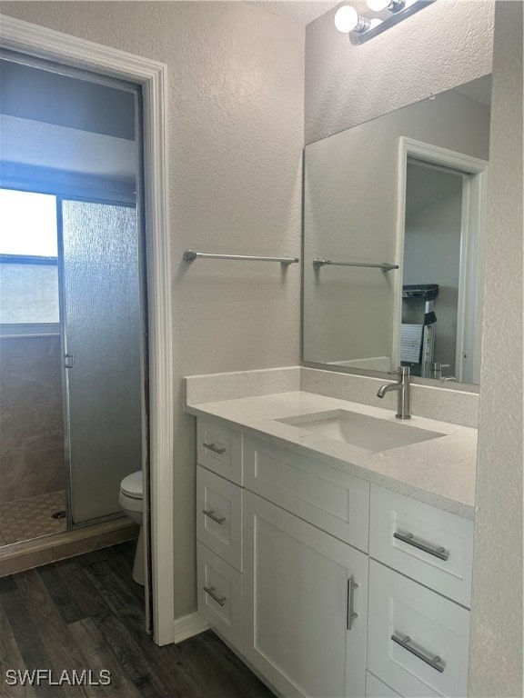 bathroom with toilet, a shower with shower door, vanity, and wood-type flooring