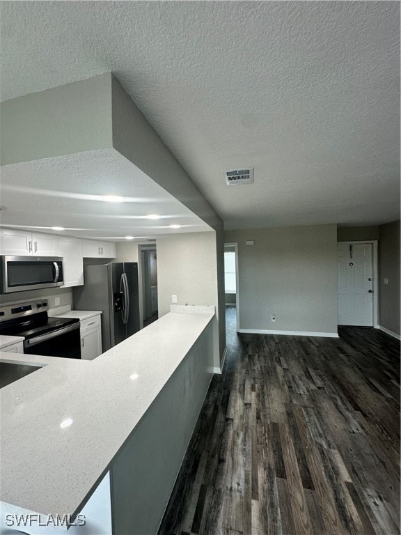 kitchen featuring a textured ceiling, kitchen peninsula, stainless steel appliances, white cabinets, and dark hardwood / wood-style floors