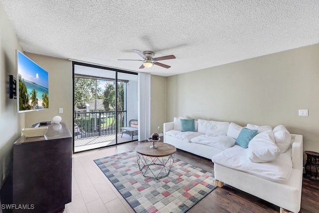 living area featuring a textured ceiling, a wall of windows, a ceiling fan, and wood finished floors