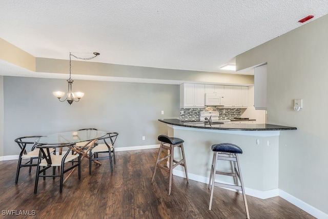 kitchen featuring white microwave, dark countertops, a kitchen breakfast bar, a notable chandelier, and tasteful backsplash