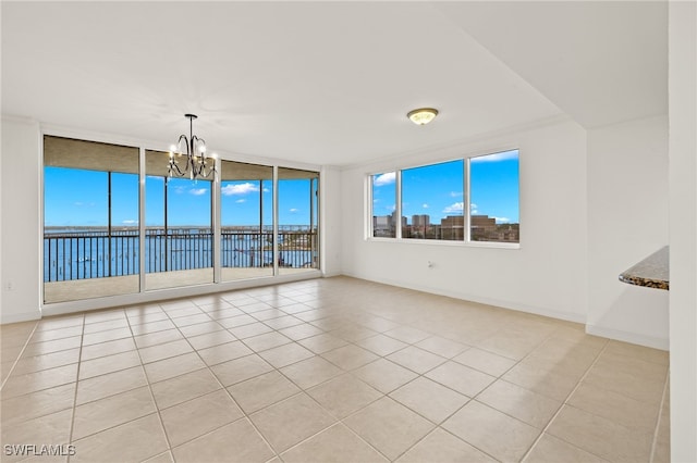 spare room featuring expansive windows, light tile patterned flooring, a notable chandelier, and a water view