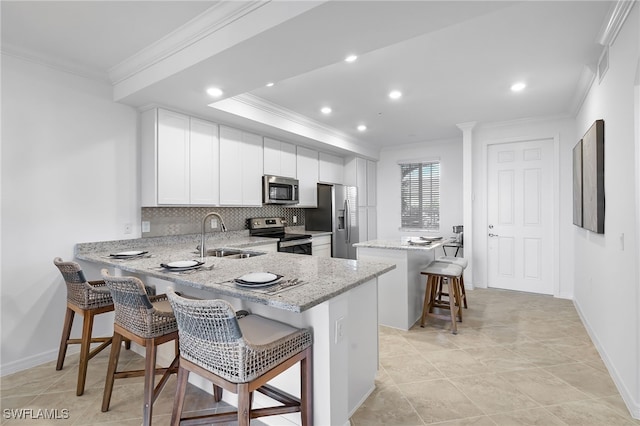 kitchen featuring kitchen peninsula, white cabinets, a breakfast bar area, sink, and stainless steel appliances