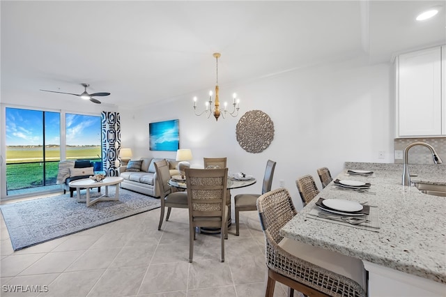 dining area with ornamental molding, sink, ceiling fan with notable chandelier, and light tile patterned floors