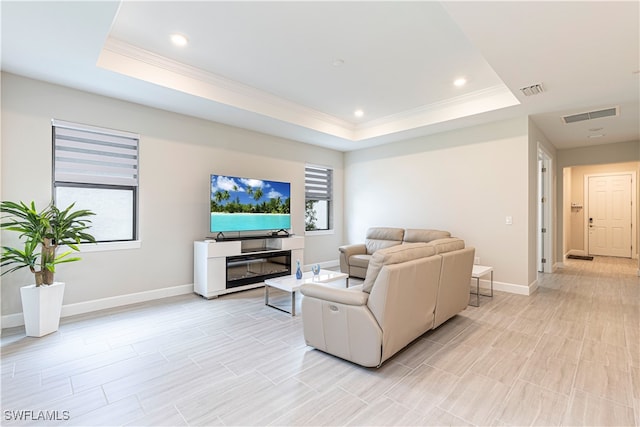 living room featuring ornamental molding, a tray ceiling, and light wood-type flooring