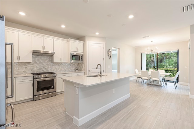 kitchen featuring a kitchen island with sink, stainless steel appliances, sink, a chandelier, and white cabinets