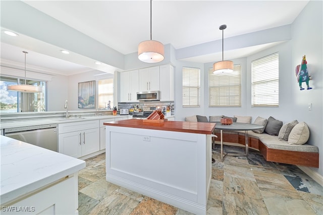 kitchen with a wealth of natural light, appliances with stainless steel finishes, hanging light fixtures, and white cabinets