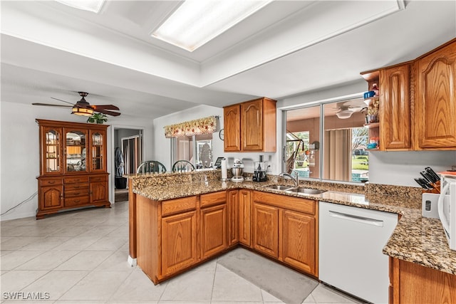 kitchen with sink, dishwasher, kitchen peninsula, dark stone countertops, and light tile patterned floors