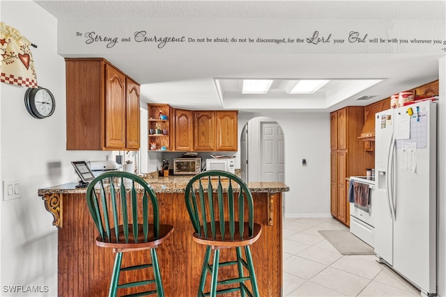 kitchen with kitchen peninsula, a breakfast bar area, light tile patterned floors, a raised ceiling, and white appliances