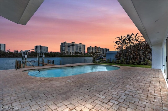 pool at dusk featuring an outdoor pool, a boat dock, boat lift, a view of city, and a patio area