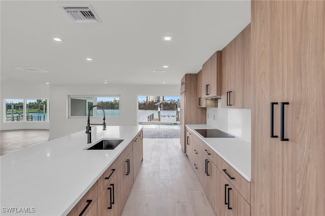 kitchen featuring black electric cooktop, sink, light brown cabinetry, light stone countertops, and light hardwood / wood-style flooring