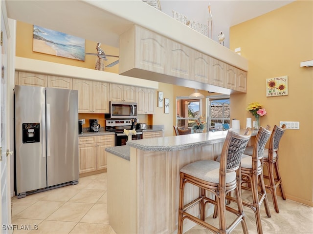 kitchen with a breakfast bar, light tile patterned flooring, kitchen peninsula, a towering ceiling, and appliances with stainless steel finishes