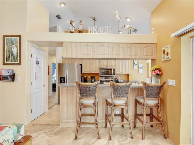 kitchen featuring a breakfast bar area, stainless steel appliances, and high vaulted ceiling