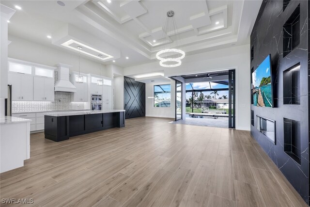 kitchen with white cabinets, a spacious island, premium range hood, light hardwood / wood-style flooring, and pendant lighting