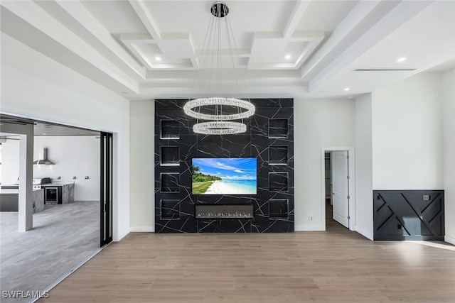 living room with an accent wall, a chandelier, coffered ceiling, and wood finished floors