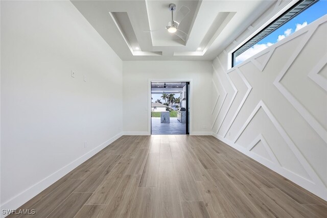 empty room with ceiling fan, a raised ceiling, and light wood-type flooring