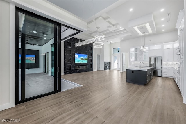 unfurnished living room with light wood finished floors, recessed lighting, a towering ceiling, coffered ceiling, and beamed ceiling