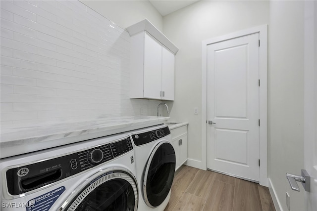 laundry area with washing machine and clothes dryer, cabinet space, light wood-style floors, a sink, and baseboards