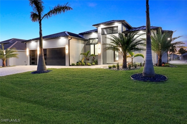 view of front of property featuring decorative driveway, a lawn, an attached garage, a standing seam roof, and metal roof