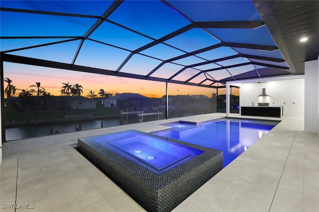 pool at dusk with an in ground hot tub, a patio, and glass enclosure