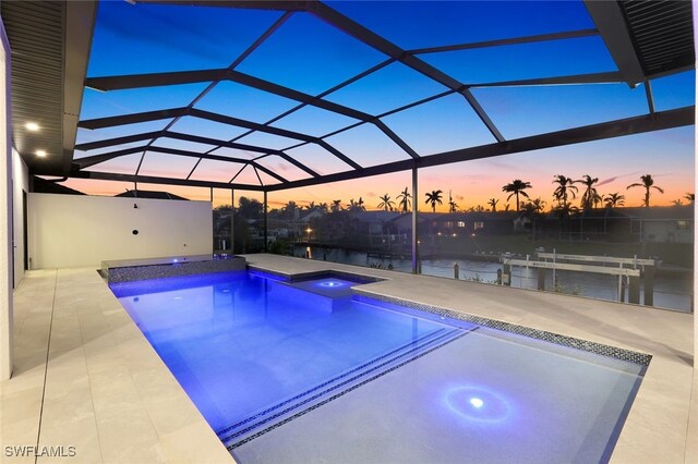 pool at dusk featuring a hot tub, a water view, a patio area, and glass enclosure