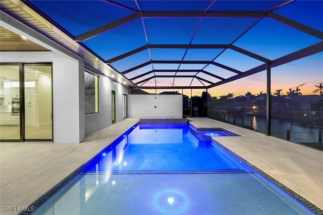 pool at dusk with a water view, an in ground hot tub, a patio, and a lanai