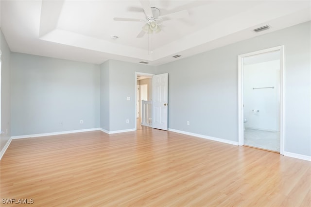 spare room with a tray ceiling, ceiling fan, and light hardwood / wood-style floors