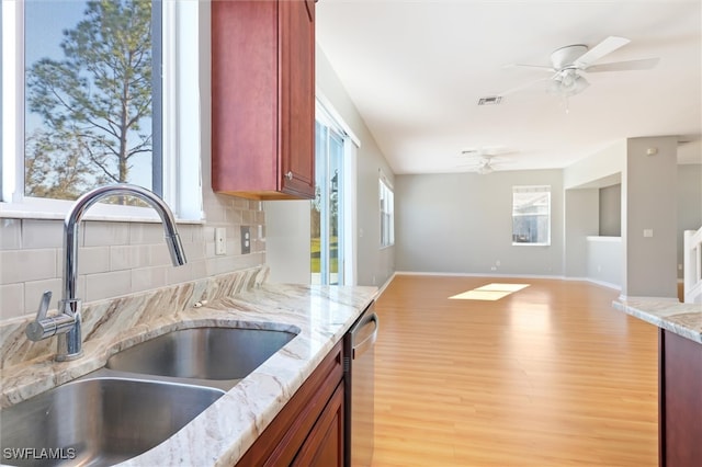 kitchen with backsplash, light stone counters, stainless steel dishwasher, sink, and light hardwood / wood-style floors