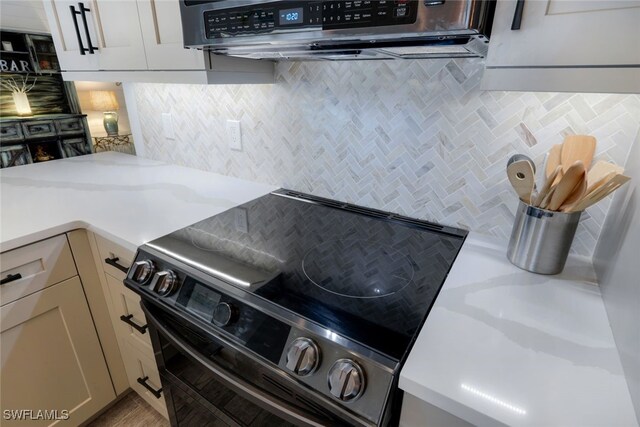 kitchen with decorative backsplash, light stone countertops, range hood, and black range with electric cooktop