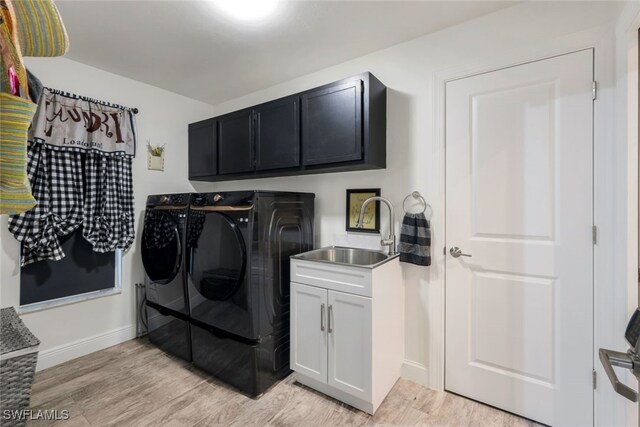 clothes washing area featuring washing machine and clothes dryer, cabinets, sink, and light hardwood / wood-style floors