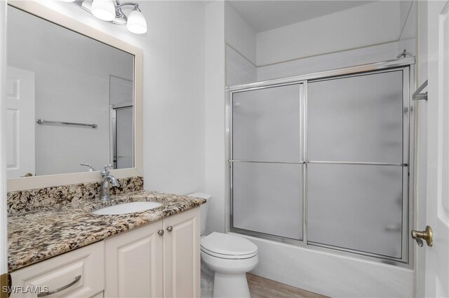 full bathroom with vanity, combined bath / shower with glass door, toilet, and wood-type flooring