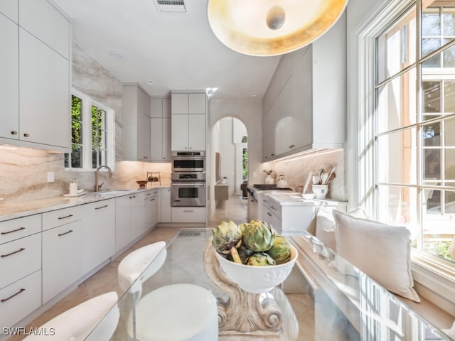 kitchen featuring stainless steel double oven, white cabinetry, tasteful backsplash, and plenty of natural light