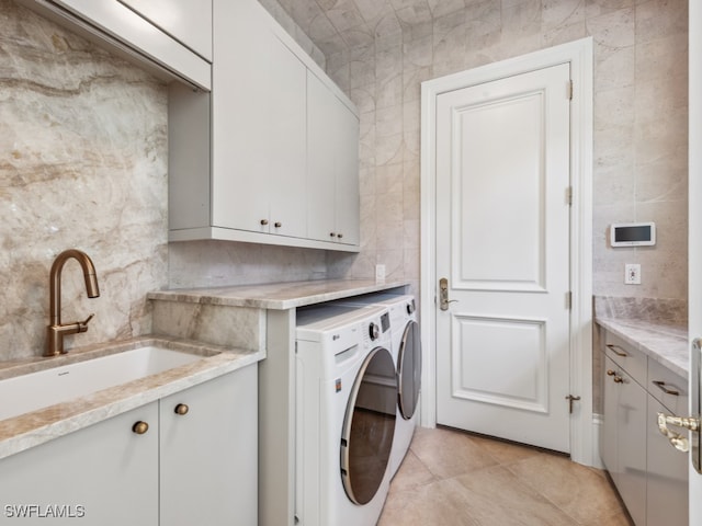 clothes washing area with washing machine and dryer, sink, tile walls, cabinets, and light tile patterned floors