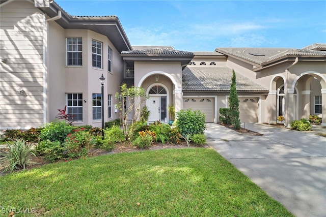 mediterranean / spanish home with a tile roof, concrete driveway, a front lawn, a garage, and stucco siding