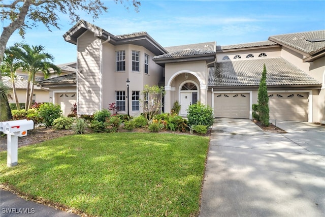 mediterranean / spanish home featuring a front yard, an attached garage, a tiled roof, and stucco siding