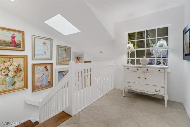 hall with tile patterned flooring, baseboards, lofted ceiling with skylight, and an upstairs landing