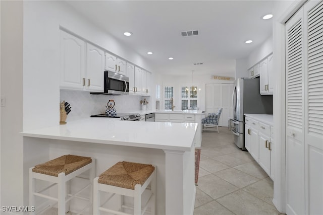 kitchen with a breakfast bar area, kitchen peninsula, stainless steel appliances, pendant lighting, and white cabinetry