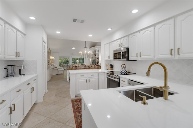 kitchen with appliances with stainless steel finishes, sink, kitchen peninsula, hanging light fixtures, and white cabinetry