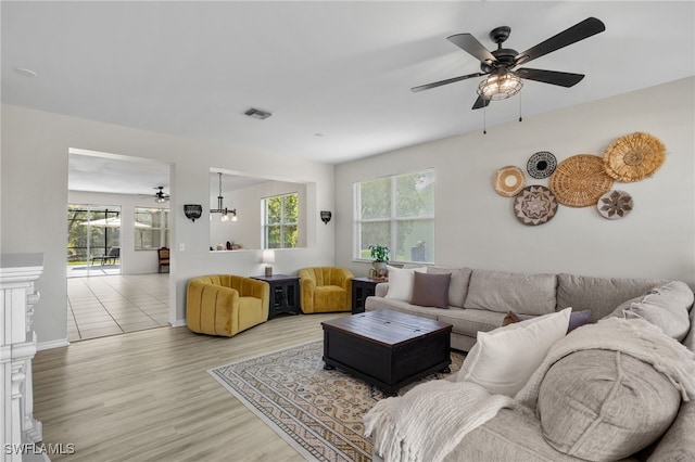 living room with ceiling fan with notable chandelier and light wood-type flooring