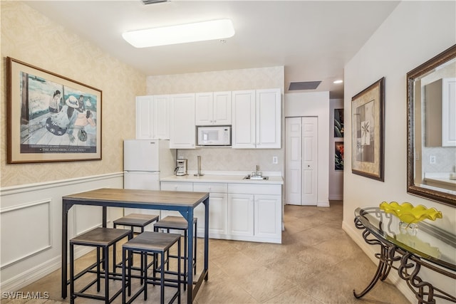 kitchen with white appliances, a breakfast bar area, sink, and white cabinets