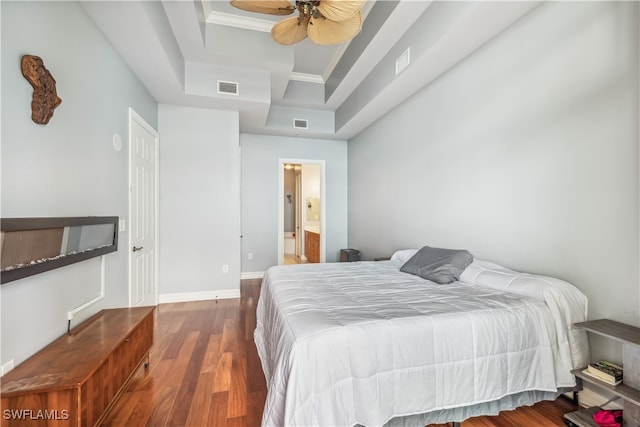 bedroom featuring connected bathroom, dark wood-type flooring, ornamental molding, a raised ceiling, and ceiling fan