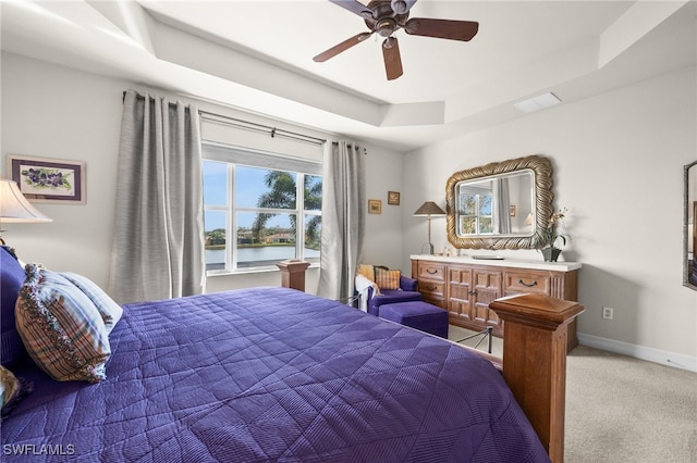 carpeted bedroom featuring a water view, a tray ceiling, and ceiling fan