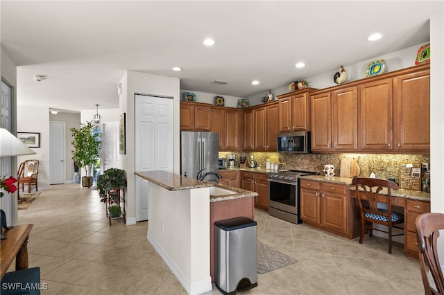 kitchen with a center island with sink, sink, appliances with stainless steel finishes, light stone counters, and tasteful backsplash