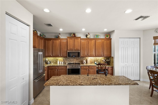 kitchen with decorative backsplash, an island with sink, light tile patterned floors, and premium appliances