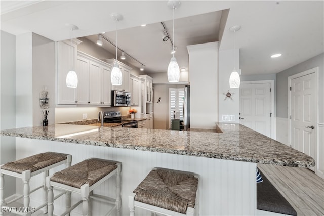 kitchen featuring white cabinetry, stainless steel appliances, a kitchen breakfast bar, kitchen peninsula, and decorative light fixtures