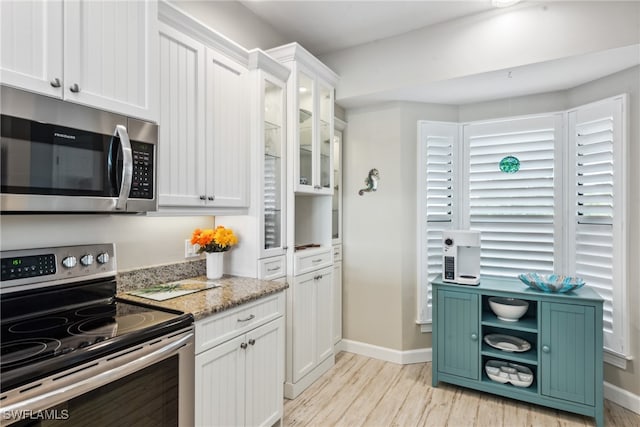 kitchen with light stone countertops, white cabinetry, appliances with stainless steel finishes, and light hardwood / wood-style flooring