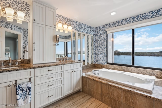 bathroom featuring vanity, a water view, wood-type flooring, and tiled tub