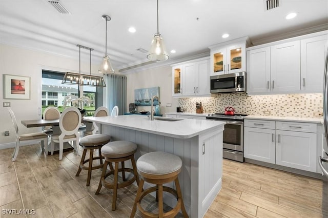 kitchen featuring appliances with stainless steel finishes, sink, decorative light fixtures, white cabinets, and an island with sink