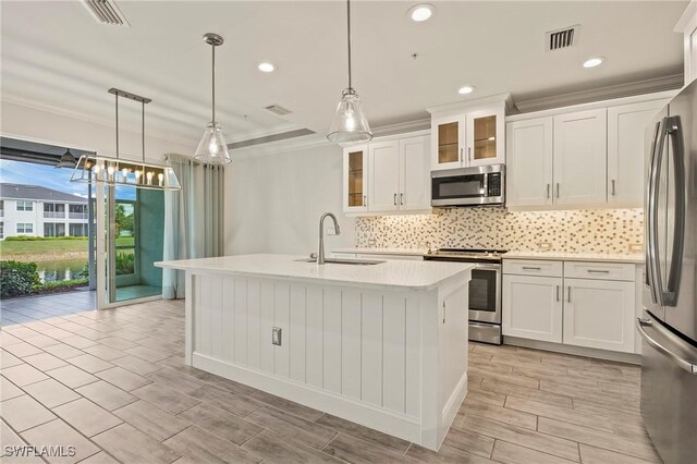 kitchen with white cabinets, a center island with sink, sink, appliances with stainless steel finishes, and decorative light fixtures