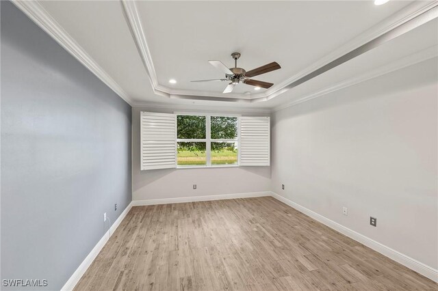 empty room with a raised ceiling, crown molding, and light hardwood / wood-style floors