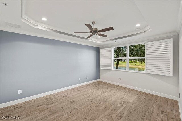 empty room with a tray ceiling, ceiling fan, crown molding, and light hardwood / wood-style floors